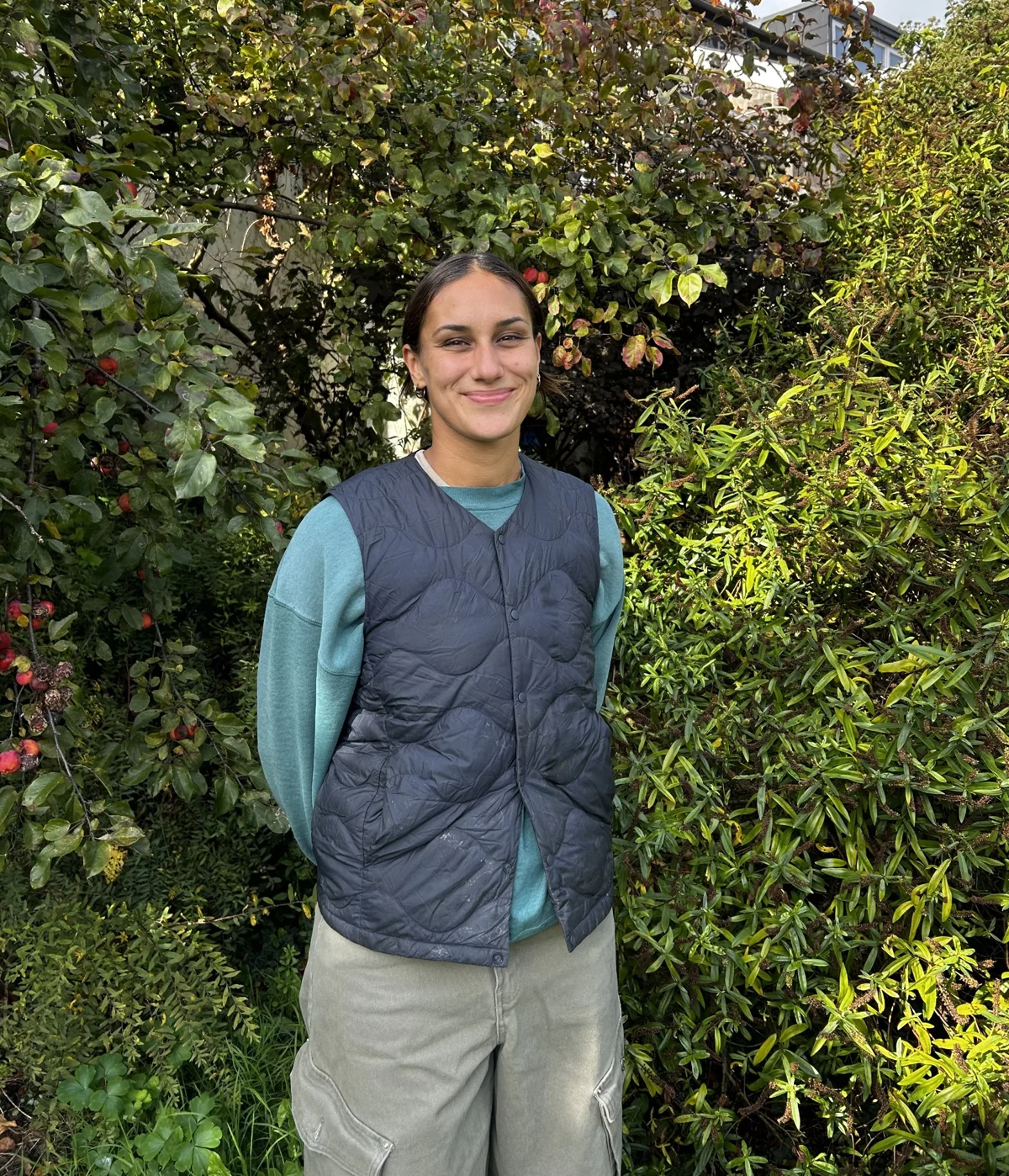 Hannah, owner of Flores Gardening, standing among leafy garden plants